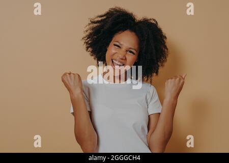 Junge, auf gelbem Hintergrund isolierte, schamhafte Frau, die Fäuste zusammenhält und Erfolge feiert Stockfoto