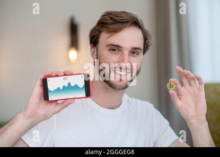 Junger bärtiger Mann, der eine Bitcoin in der Hand hält Stockfoto