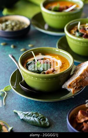 Nahaufnahme einer Schüssel Butternut-Kürbissuppe, die fertig zum Essen ist, mit anderen Schüsseln Suppe dahinter. Stockfoto