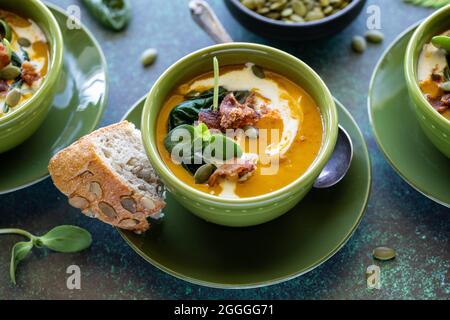 Schauen Sie aus nächster Nähe in eine Schüssel mit cremiger Butternut-Kürbissuppe, serviert mit rustikalem Kürbiskernbrot. Stockfoto