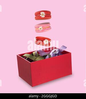 Bunte Makronen oder französische Makronen schweben auf einer roten Geschenkbox mit bunten Bändern. Isolation auf rosa Hintergrund. Schwebendes foo Stockfoto