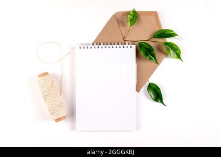 Notizbuch, Umschlag aus recyceltem Papier und Spule aus einfachem grobem Faden liegen auf weißer Oberfläche mit einem Zweig grüner Pflanze. Ökologie-Konzept, recyclebar, nein war Stockfoto