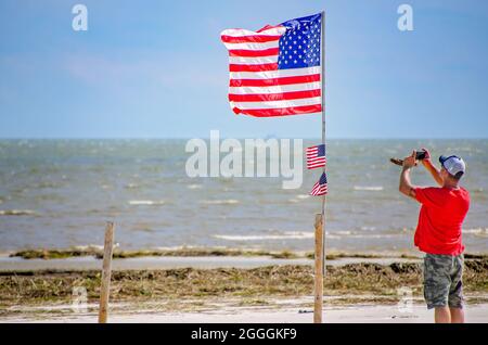 Ein Mann nutzt sein Mobiltelefon, um eine amerikanische Flagge inmitten von Trümmern am Strand nach dem 31. August 2021 in Gulfport, Mississippi, zu fotografieren. Stockfoto
