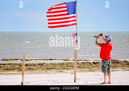 Ein Mann nutzt sein Mobiltelefon, um eine amerikanische Flagge inmitten von Trümmern am Strand nach dem 31. August 2021 in Gulfport, Mississippi, zu fotografieren. Stockfoto