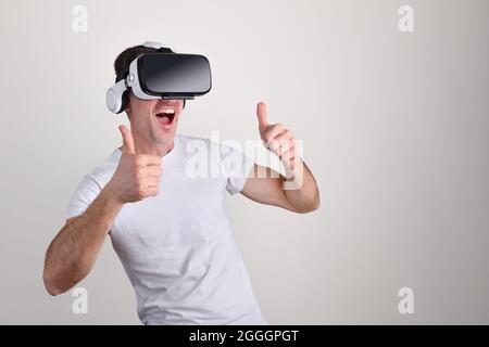 Mann mit Spaß in weißen T-Shirt-Händen gekleidet mit ok-Geste mit Virtual-Reality-Brille und weißen isolierten Hintergrund Stockfoto