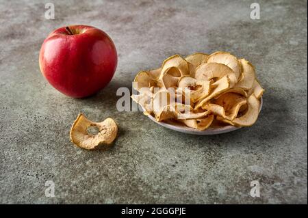 Dehydrierte Apfelchips auf dem Teller und Apfelfrüchte auf Holzhintergrund. Nahaufnahme Stockfoto