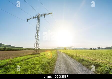 Stromleitung in ländlicher Landschaft mit landschaftlich reizvollen Sonnenstrahlen und Streulicht, die grüne, erneuerbare Energie symbolisieren Stockfoto