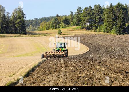 John Deere Traktor und Pflug arbeiten auf geerntetem Feld an einem schönen sonnigen Tag im Frühherbst. Salo, Finnland. 29. August 2021. Stockfoto