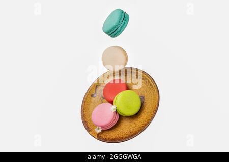 Eine orangefarbene Keramikplatte mit farbenfrohen Macaroonsi-Fallbewegungen. Konzepte zur Levitation von Lebensmitteln. Isolation auf weißem Hintergrund. Stockfoto