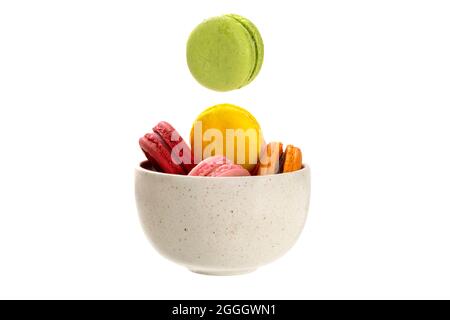 Ein grüner Makronen, der auf einer Keramikschale voller farbenfroher Makronen schwimmt. Isolation auf weißem Hintergrund. Levitation Food Konzept. Stockfoto