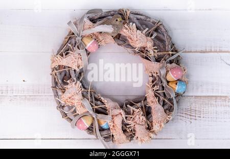 Handgefertigter Osterkranz aus Zweigen und Bändern mit niedlichem Vogel und Holzeiern. Stockfoto