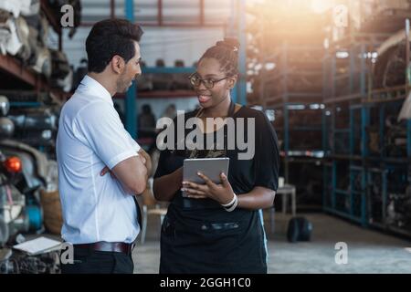 Ingenieur-Controller überprüfen und sprechen mit afrikanischen Frau arbeiten auf Tablet in der Fabrik der alten Auto-Ersatzteile Stockfoto