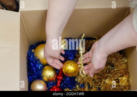 Eine Frau nimmt Weihnachtsdekorationen aus einer Schachtel. Weihnachtskugeln, Lametta, Girlanden. Frohe Weihnachten, Frohes neues Jahr. Stockfoto