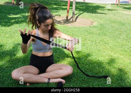 Keine binäre Person, die muay thai Bandagen trägt, sitzt auf Gras in einem Park. Stockfoto