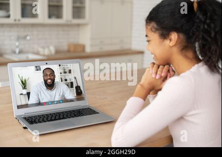 Rückansicht einer afroamerikanischen Frau, die mit ihrem männlichen Freund oder Kollegen am Schreibtisch im Heimbüro einen Videoanruf abruft. Videokommunikation, virtuelles Meeting-Konzept Stockfoto