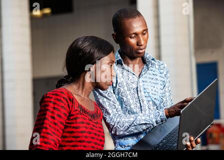 Junger afrikanischer Geschäftsmann zeigt den Projektplan mit dem Finger auf dem Laptop-Bildschirm, während eine Frau lächelt Stockfoto
