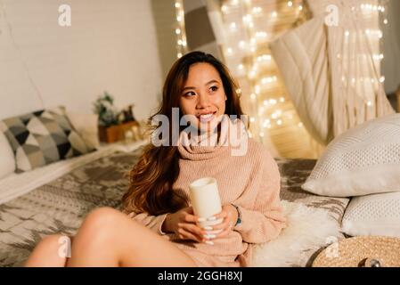 Lächelnde junge asiatische Frau mit einem weihnachtsgeschenk-Box in der Nähe von weihnachtsbaum Stockfoto