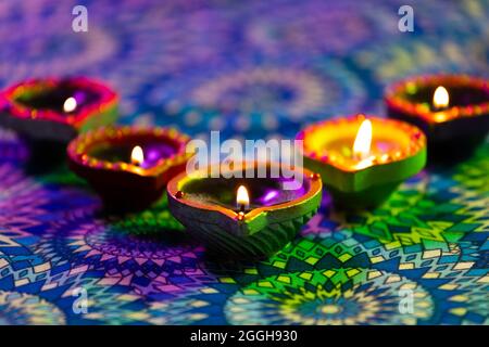 Brennende Kerzen in kleinen dekorativen Tontöpfen, die auf gemustertem Tischtuch brennen Stockfoto