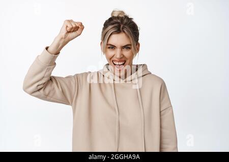 Junge Frau, die Unterstützung zeigt, die Faust schüttelt und schreit, für das Team wurzelt, Sportspiele anschaut, vor weißem Hintergrund steht Stockfoto