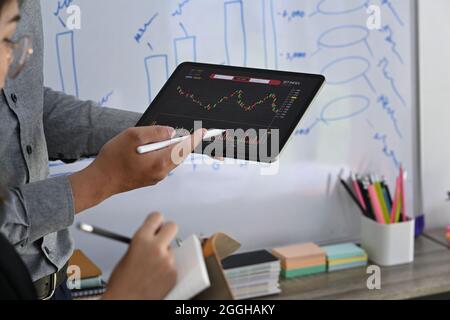 Zwei Anleger, die Aktienmarktinvestitionen gemeinsam über digitale Tablets im Büro analysieren. Stockfoto