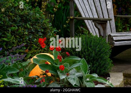 Stilvolles, beleuchtetes Globenlicht, das in der Dunkelheit beleuchtet und leuchtet, blühende Pflanzen und Holzsitze in einem privaten Garten in der Abenddämmerung - Yorkshire, England, Großbritannien Stockfoto