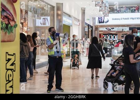 Jerusalem, Israel. September 2021. Ein engagierter Coronavirus-Inspektor kündigt Anweisungen an und erinnert die Käufer daran, Gesichtsmasken in der inneren Malcha Shopping Mall in Jerusalem zu tragen, während Israel eine vierte Welle von COVID-19, die hauptsächlich aus der Delta-Variante besteht, kämpft. Kredit: Nir Alon/Alamy Live Nachrichten Stockfoto