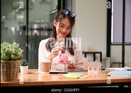 Junge asiatische Frau, die Münzen in ein Sparschwein legt. Investitionen oder Einsparungen für zukünftiges Wachstum. Stockfoto