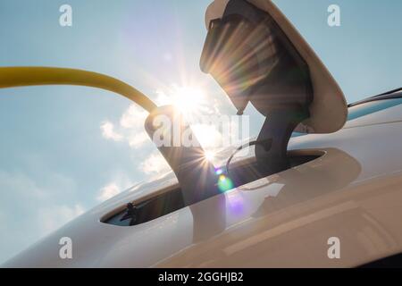 Frau, die das Ladegerät für Elektroautos gegen Sonne und blauen Himmel ansteckt. Stockfoto