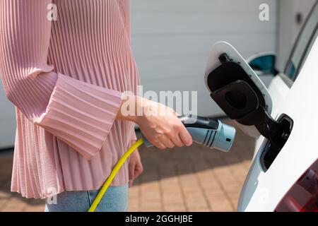 Frau, die einen Ladestecker oder ein Ladegerät in ein weißes Elektroauto steckt Stockfoto