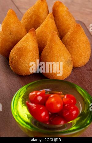 Traditioneller brasilianischer frittierter Snack mit Huhn, bekannt als „Coxinha“, und Paprika mit kleinem Schnabel, Brasilien, genannt „Pimenta Biquinho“. Stockfoto