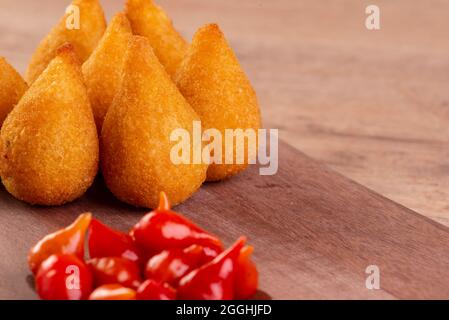 Traditioneller brasilianischer frittierter Snack mit Huhn, bekannt als „Coxinha“, und Paprika mit kleinem Schnabel, Brasilien, genannt „Pimenta Biquinho“. Stockfoto