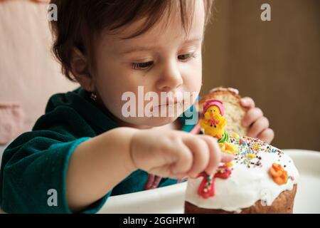 1 Jahr altes Baby altes Mädchen isst Panettone. Niedliche kleine kaukasische Mädchen hält Osterkuchen. Ein Jahr Alte Baby Entwicklung Stockfoto