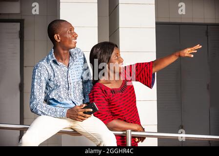 Schöne Frau, die draußen in traditioneller Kleidung steht und ihrem Kollegen lächelnd etwas zeigt. Stockfoto