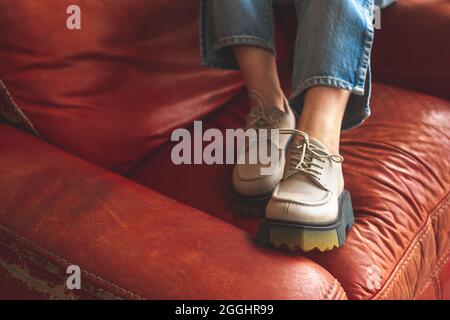 Vintage-Mode, weibliche Beine in Denim-Jeans und Urban-Sneakers auf dem Hintergrund eines roten alten Sessels im Retro-Stil, Nahaufnahme Stockfoto