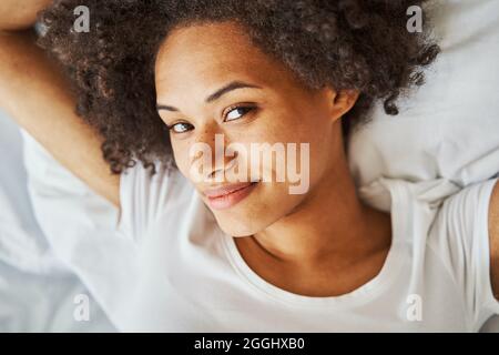 Weibchen mit lockigen Haaren, die die Zeit im Bett verflüchtigen Stockfoto