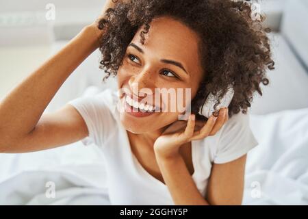 Fröhliche, hübsche Dame in kabellosen Kopfhörern schaut weg Stockfoto