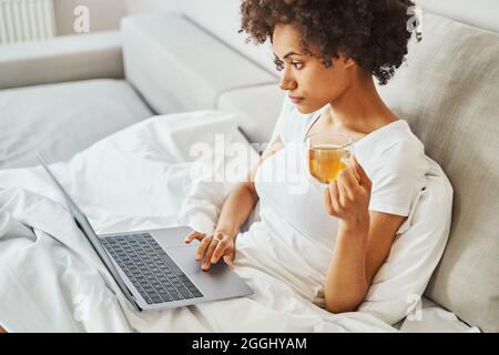 Junge Frau benutzt ihren tragbaren PC im Bett Stockfoto