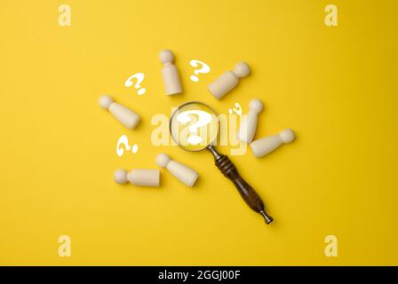 Holzmänner und eine Lupe auf gelbem Hintergrund. Rekrutierungskonzept, Suche nach talentierten und fähigen Mitarbeitern, Karriereentwicklung, Flat Lay Stockfoto