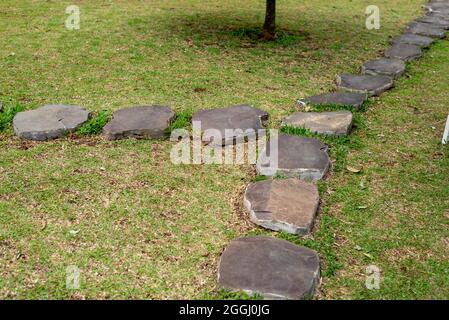Steinweg auf einem grünen Rasen. Der Weg pflasterten einzelne Steine zwischen einem grünen Gras. Stockfoto
