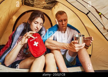 Der Mann trinkt einen Becher Kaffee, während die Freundin einen Kasten mit Medikamenten hält, während sie auf Camping gehen Stockfoto