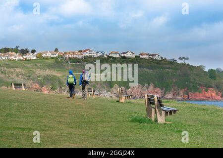 Paar gehen, Rückansicht von Menschen, die auf dem South West Coast Path in Richtung Broadsands Beach in Torbay, South Devon, England, Großbritannien, gehen Stockfoto