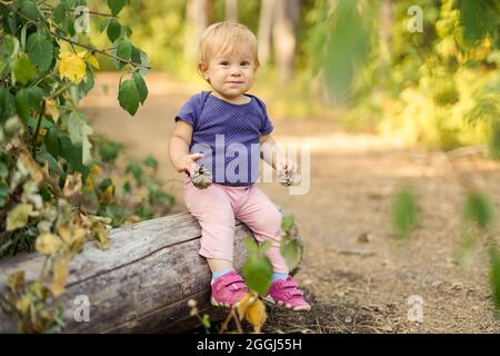 Kleines Kind, das auf einem umgestürzten Baum im Wald sitzt Stockfoto
