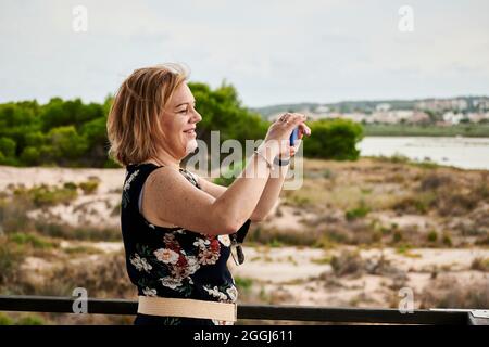 Eine Frau mittleren Alters fotografiert mit ihrem Telefon in einem Naturpark Stockfoto