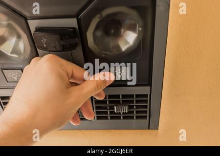 Die Hand des Mannes drückt mit dem Finger auf die Taste, um das Licht auf dem Bedienfeld für den Passagier im Bus aus der Nähe einzustellen und einzuschalten. Stockfoto