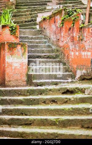 Vertikale Aufnahme der alten Treppe, teilweise mit Moos bedeckt und von orangen Wänden umgeben. Stockfoto