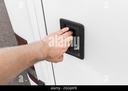 Die Hand eines Mannes öffnet oder schließt den Gepäckraum eines Fahrzeugs, Autos oder Busses am Türgriff. Stockfoto