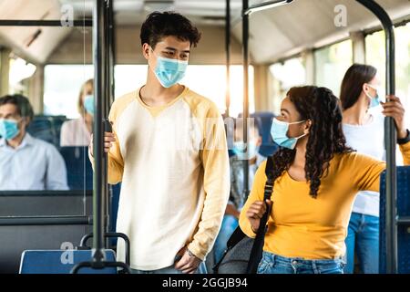 Verschiedene multikulturelle Menschen tragen Gesichtsmasken und unterhalten sich im Bus Stockfoto