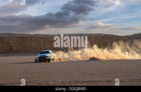 Ein schwarzes Auto oder ein Pickup-Truck treibt einen Sand und spritzt Sand in der Luft und in der Dasht e lut- oder sahara-Wüste herum. Stockfoto