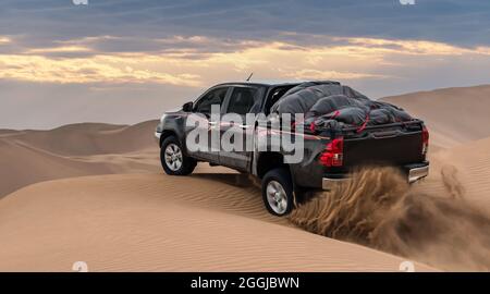 Ein weißer Pickup-Truck fährt von einer Sanddüne hoch und spritzt Sand in die Luft und in die Dasht e lut- oder sahara-Wüste. Stockfoto