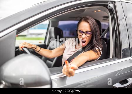 Die wütende weibliche Fahrerin zeigt während der Hauptverkehrszeit den Mittelfinger in einen Rückspiegel. Stockfoto